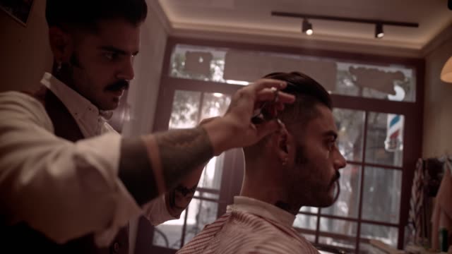 Young-stylish-old-fashioned-barber-with-tattoos-cutting-customer's-hair
