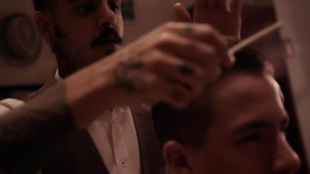 Young-stylish-hairdresser-with-tattoos-and-mustache-styling-man's-hair