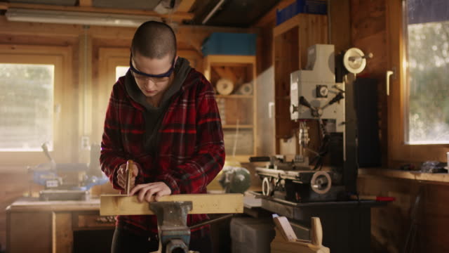 Young-gritty-woman-sawing-wood-in-workshop