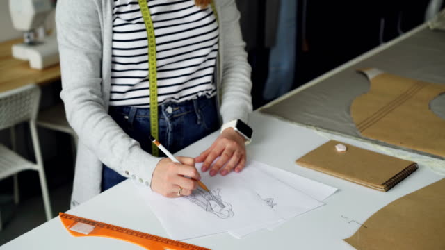 Tilt-up-shot-of-creative-clothing-designer-concentrated-on-drawing-sketch-of-women's-garment-on-piece-of-paper-with-pencil.-Creating-fashionable-clothes-concept.
