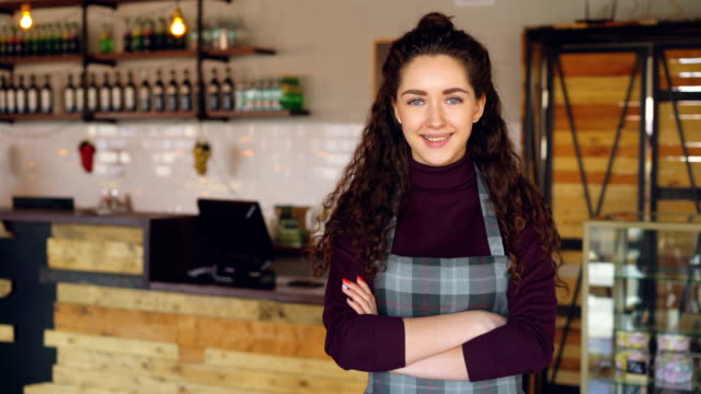 Portrait-of-attractive-confident-woman-small-business-owner-standing-in-her-opening-coffee-shop-and-smiling-looking-at-camera.-Coffee-house-interior-in-background.