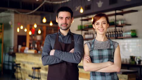 Portrait-of-two-cheerful-waiters-standing-inside-cozy-cafe,-smiling-and-looking-at-camera.-Successful-business,-happy-attractive-people-and-food-service-concept.