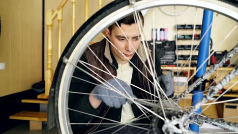 Professional-mechanic-man-is-repairing-bicyce-wheel-in-modern-workplace-with-spare-parts-and-special-equipment.-Maintenance,-people-and-small-business-concept.