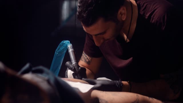 Professional-tattooist-using-tattoo-machine-and-working-on-client's-tattoo