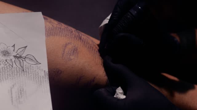 Artista-del-tatuaje-utilizando-la-máquina-del-tatuaje-y-el-dibujo-diseño-en-piel