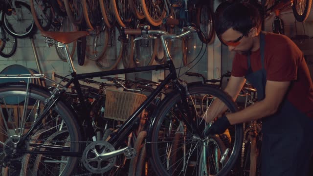 theme-small-business-bike-repair.-A-young-Caucasian-brunette-man-wearing-safety-goggles,-gloves-and-an-apron-uses-a-hand-tool-to-repair-and-adjust-the-bike-in-the-workshop-garage