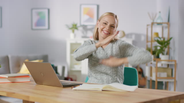 Beautiful-Cheerful-Blonde-Does-Funny-Dance-Routine-while-Sitting-at-Her-Desk-in-the-Living-Room.-Happy-Woman-Doing-Celebratory-Dancing.