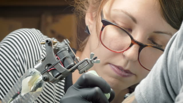 Mujer-joven-tatuador-darle-a-alguien-un-tatuaje-en-4K