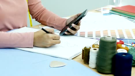 Hand-der-Schneiderin-für-Kleid-Design-auf-Papier-zeichnen-hautnah.-Kleid-mit-Smartphone-zum-inspirieren-mit-ihrem-Design-Hersteller.