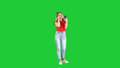 Beautiful-young-woman-using-mascara-and-looking-in-her-smartphone-on-a-Green-Screen,-Chroma-Key