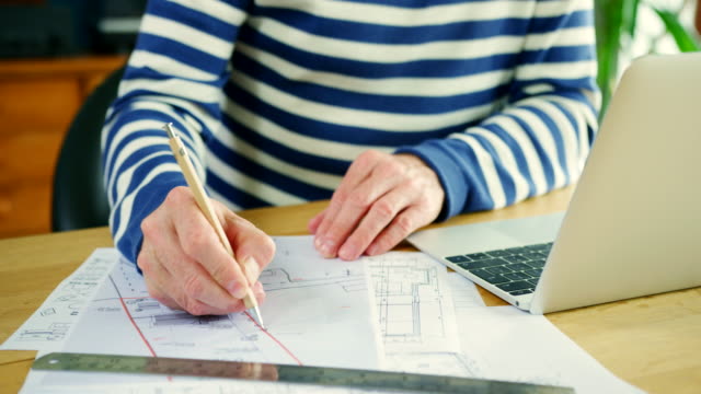 Architect-Working-On-Construction-Design-Blueprints-At-His-Desk