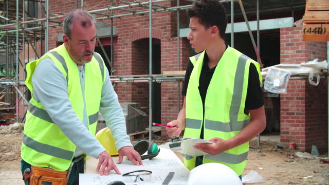 Builder-On-Site-Discussing-Work-With-Male-Apprentice