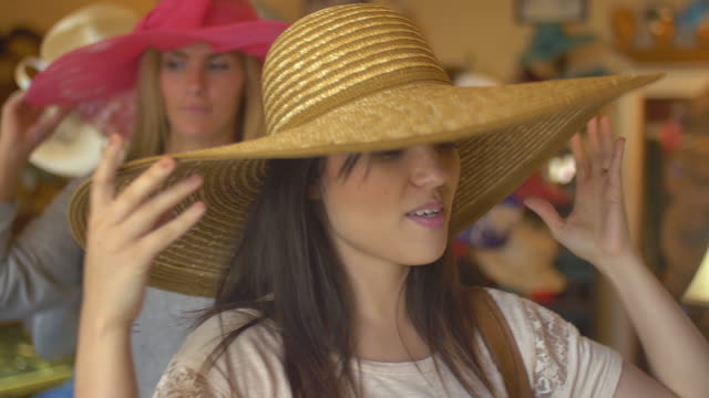 Close-up-of-two-young-women-trying-on-hats-in-a-store