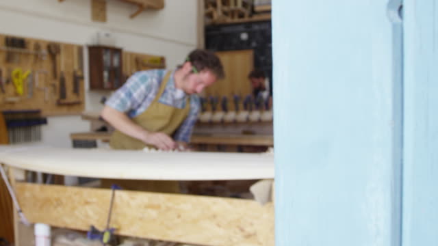 Man-Shaping-Custom-Surfboard-en-el-taller-filmado-en-la-cámara-roja