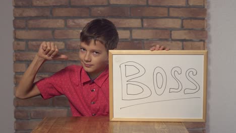 child-sitting-at-the-desk-holding-flipchart-with-lettering-boss-on-the-background-red-brick-wall