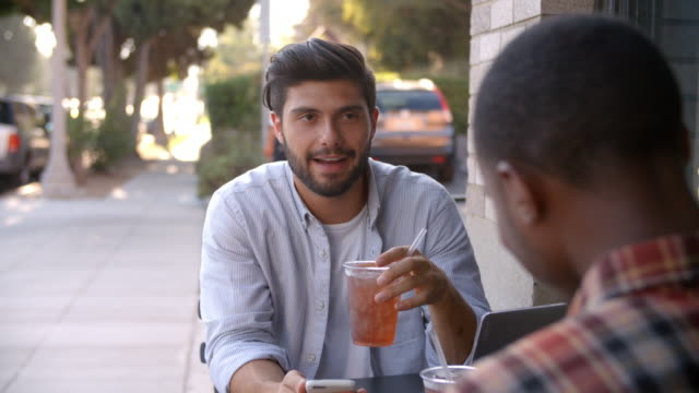 Zwei-erwachsenen-männlichen-Freunden-sprechen-über-kalte-Getränke-vor-café