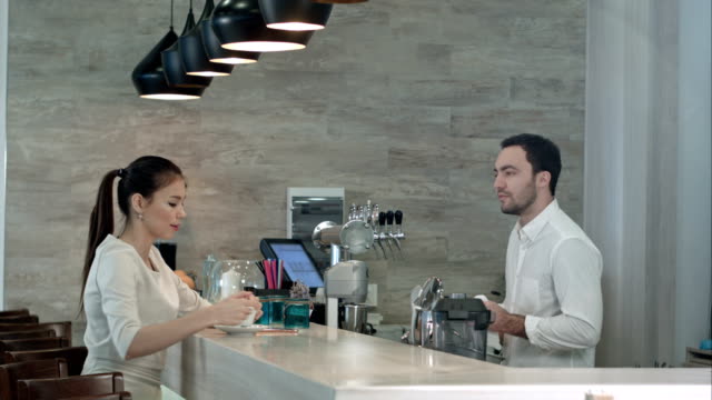 Smiling-barista-and-young-pretty-woman-talking-in-coffee-shop