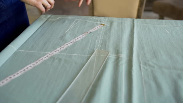 Seamstress-and-fashion-designer-at-work.-Young-woman-draw-chock-on-the-cloth-in-tailor-studio