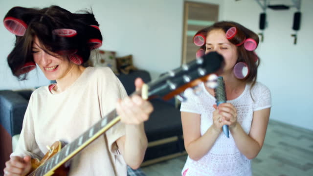 Zwei-lustige-Mädchen-singen-mit-Kamm-und-spielen-E-Gitarre-Tanz,-singen-und-Freude-zu-Hause-haben