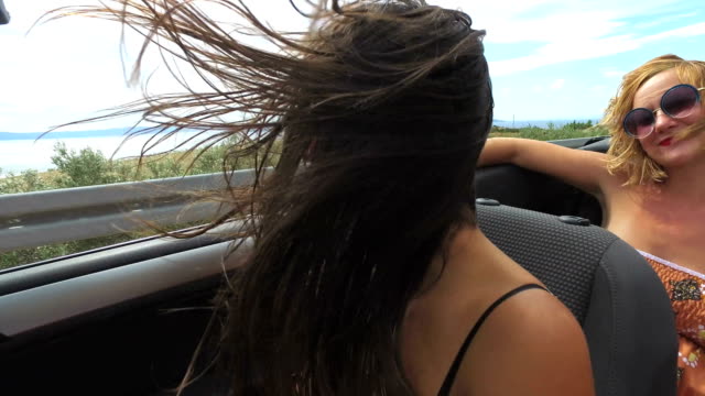 Two-attractive-women-riding-in-cabriolet-along-dalmatian-coast