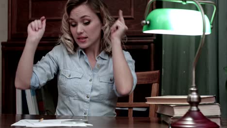 Pretty-young-woman-sitting-at-her-desk-with-books-and-having-funny-little-dance