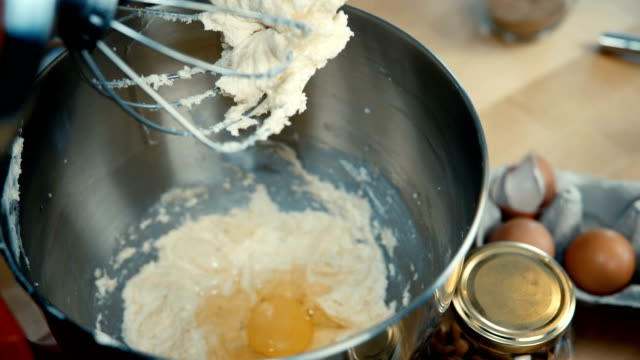 Close-up-view-of-female-hands-adds-the-egg-and-turns-on-the-mixer.-Woman-cooking-the-dough-in-the-bowl-on-the-kitchen