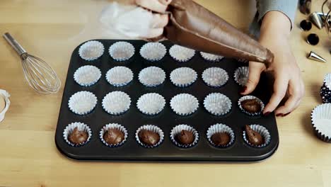 Close-up-view-of-female-hands-putting-the-dough-into-the-wrappers,-paper-cups-for-cupcakes,-using-pastry-bag