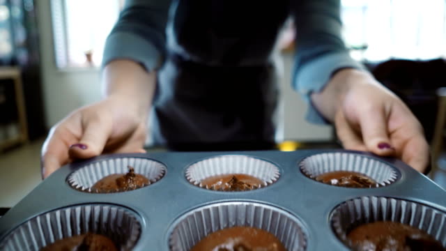 View-inside:-young-woman-open-oven-and-putting-in-baking-tray-for-cupcakes.-Female-dancing-while-waiting-the-desserts