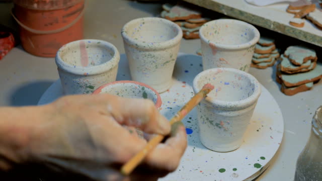 Professional-male-potter-painting-mugs-in-pottery-workshop