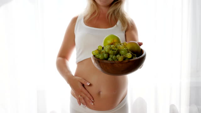 smiling-woman-with-naked-abdomen-keeps-dish-with-fresh-fruits-and-look-in-camera