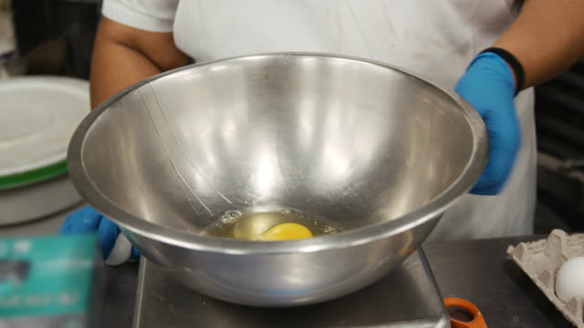 Baker-breaking-eggs-into-a-mixing-bowl,-mid-section