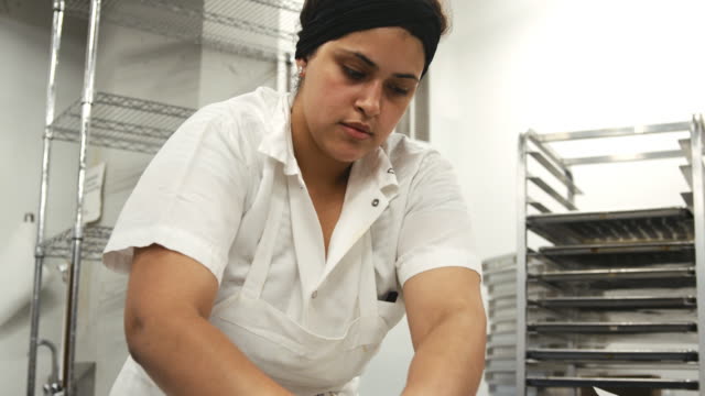 Hispanic-woman-cutting-cookie-dough-at-a-bakery,-close-up
