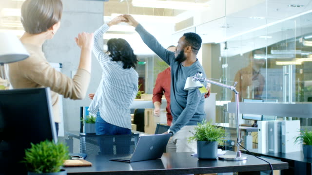 Diverse-Group-of-Young-Women-and-Men-Dance-and-Have-Fun-in-the-Modern-Office.-Black-Young-Man-Spins-Beautiful-Hispanic-Woman.