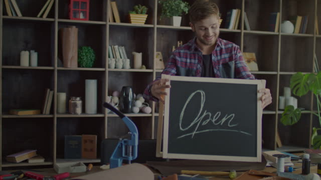 Happy-business-owner-putting-open-sign-on-table-in-small-shop