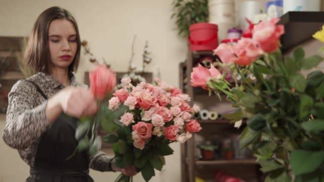 Junge-und-hübsche-Frau-macht-einen-Strauß-Rosen-für-den-Verkauf-in-einem-Blumenladen