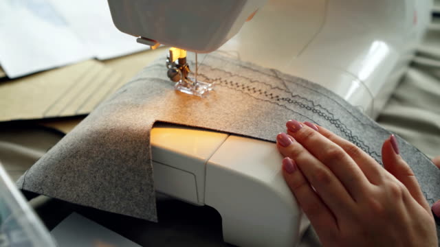 Close-up-shot-of-working-sewing-machine,-fabric-and-manicured-female-hand.-Clothes-manufacturing-process-concept.-Light-soft-colours