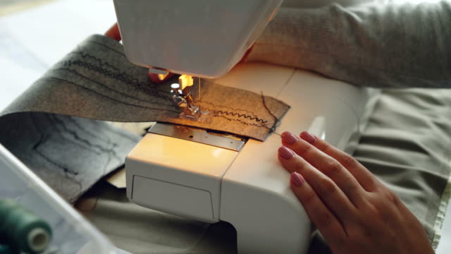 Close-up-view-of-modern-electric-sewing-machine-working-stitching-piece-of-fabric.-Girl's-manicured-hand-and-colorful-sewing-threads-are-visible.