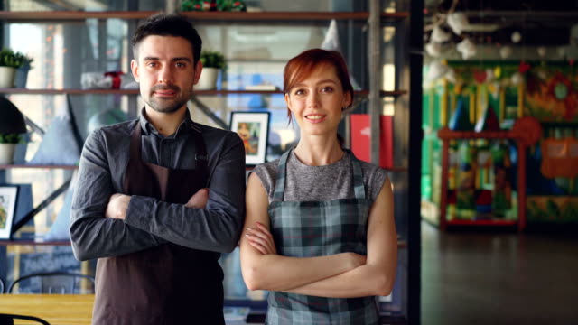 Portrait-of-two-proud-small-business-owners-standing-inside-new-spacious-cafe-and-smiling.-Successful-business-start-up,-happy-people-and-food-service-concept.
