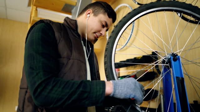 Konzentrierte-Mechaniker-ist-mit-speziellen-Werkzeugen-Speichen-auf-Fahrrad-Rad-Befestigung,-während-der-Wartung-Motorrad-und-Musik-über-Kopfhörer-hören.-Pflege-und-Beruf-Konzept.