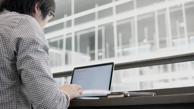 Hombre-de-negocios-asiático-joven-usando-la-computadora-portátil-en-el-espacio-de-trabajo-con-el-smartphone-y-el-portátil-en-el-escritorio-de-madera.-Macho-mano-escribiendo-en-el-teclado-del-ordenador-portátil.-Estilo-de-vida-independiente-en-concepto-