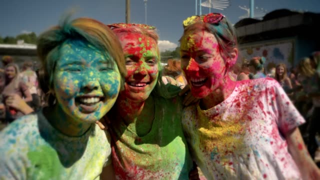 Tres-jóvenes-amigas-multiétnicas-se-ríen-en-el-festival-de-holi-en-horario-diurno-en-verano,-el-concepto-de-la-amistad,-el-concepto-del-color