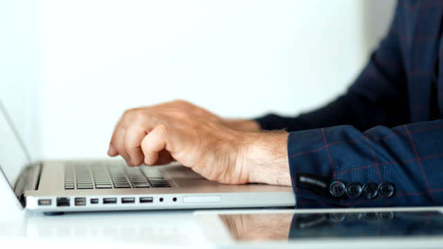 Close-up-of-businessman's-hands-typing-on-laptop-in-white-office
