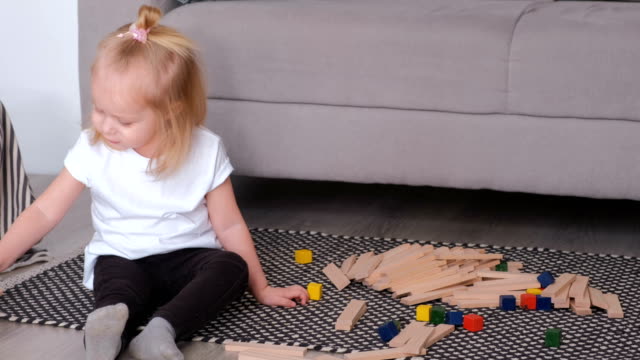 Encantadora-rubia-niña-jugando-bloques-de-madera-sentada-cerca-del-sofá.