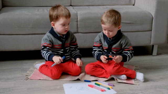 Zwei-Twin-Brüder-Kleinkinder-ziehen-zusammen-Markierungen-auf-dem-Boden-sitzen.
