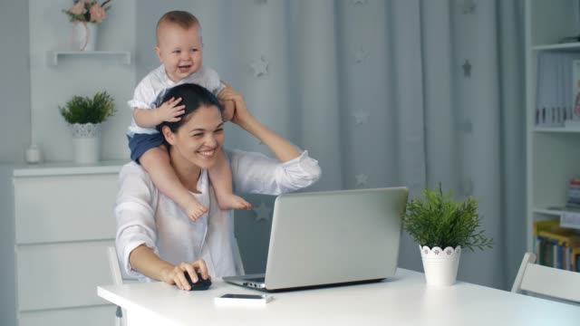 Madre-con-bebé-trabajando-en-ordenador-portátil-en-casa