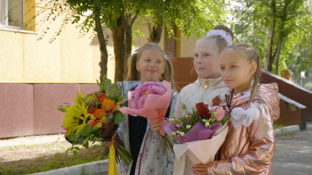 Colegialas-alegres-con-flores-hablando-y-juntos-en-pie-cerca-de-la-escuela