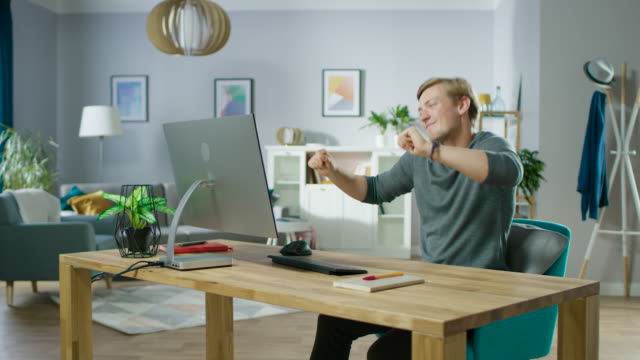 Portrait-of-the-Handsome-Young-Man-Dances-while-Sitting-Before-His-Computer.-Young-Man-Having-Fun-at-Home.