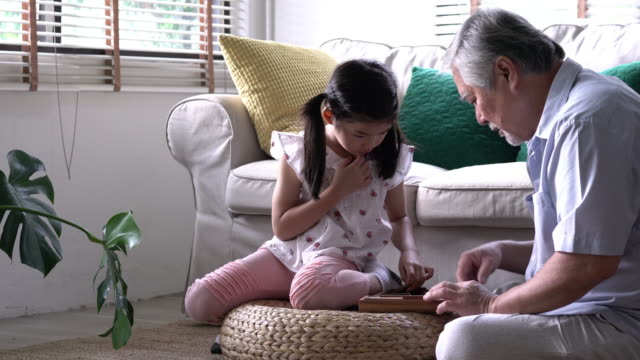 Senior-man-and-kids-girl-playing-puzzle-games-together-in-living-room-at-home.-Concept-of-caucasian-family,-education,-growing-learn-and-development-of-age.-4k-resolution.