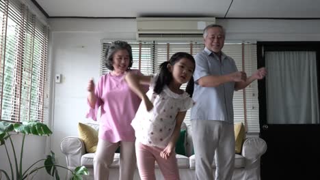 Paar-Senioren-und-Kinder-Mädchen-tanzen-zusammen-im-Wohnzimmer-zu-Hause.-Konzept-der-glückliche-Familie-begeistern-Party,-psychische-Gesundheit-und-positive-Psychologie.-4-k-Auflösung.
