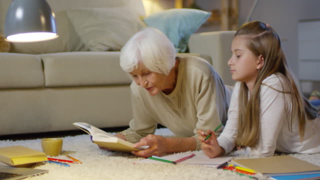 Liebevolle-Oma-macht-Hausaufgaben-mit-Mädchen-auf-dem-Boden